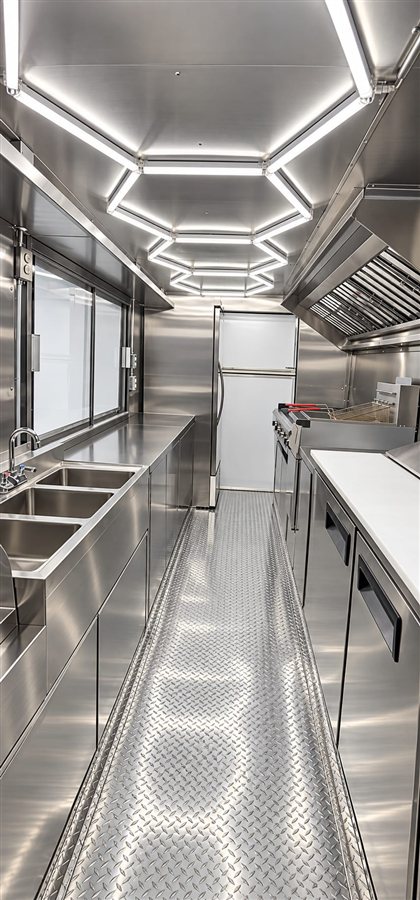 Empty stainless steel food truck kitchen with hexagon LED ceiling lighting, reach-in fridge and three-basin sink
